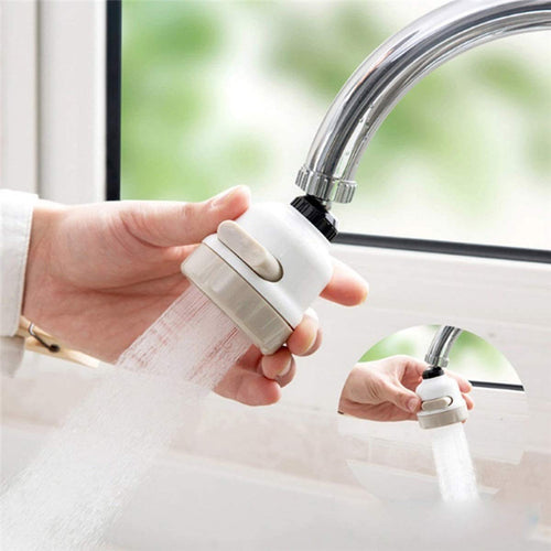 Hand holding a white faucet attachment with water flowing, with another attachment on a sink.
