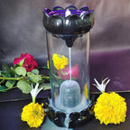 Flower arrangement with a transparent container featuring a purple top and black base, surrounded by flowers on a dark background.
