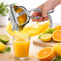 Hand using a manual juicer to extract juice from an orange, with a glass of orange juice and citrus fruits on a wooden surface.