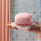 Pink handheld shower scrubber with soap suds in a hand against a tiled bathroom background